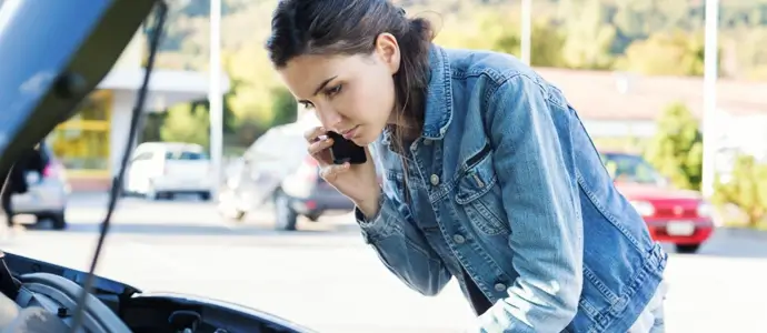 Young woman calling a car assistance service with her smartphone, her car has broken down