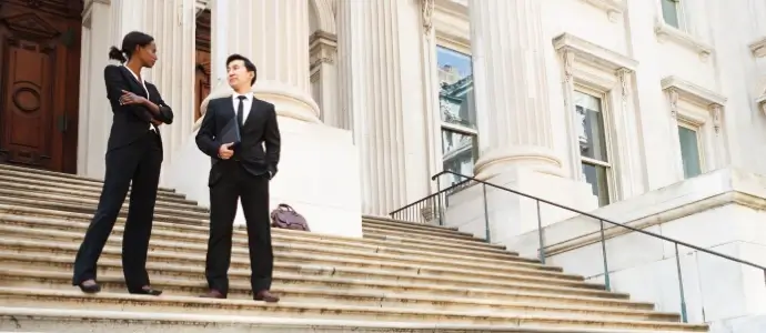A well dressed man and woman converse on the steps of a legal or municipal building.