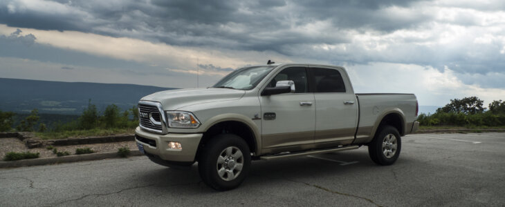 Pickup truck parked on a scenic overlook with mountains in the distance and dramatic storm clouds or cloudscape. Headlights are on for the dark stormy atmosphere.